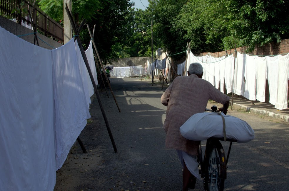An old washerman leaves on his cycle to deliver the clothes.