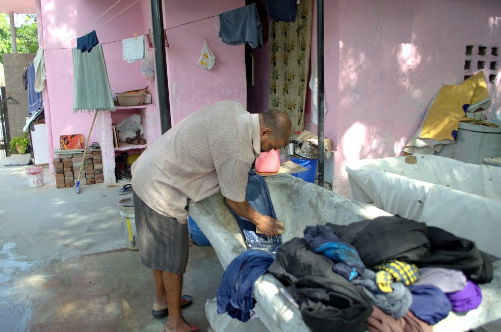 A washerman scrubbing clothes with detergent before washing them.