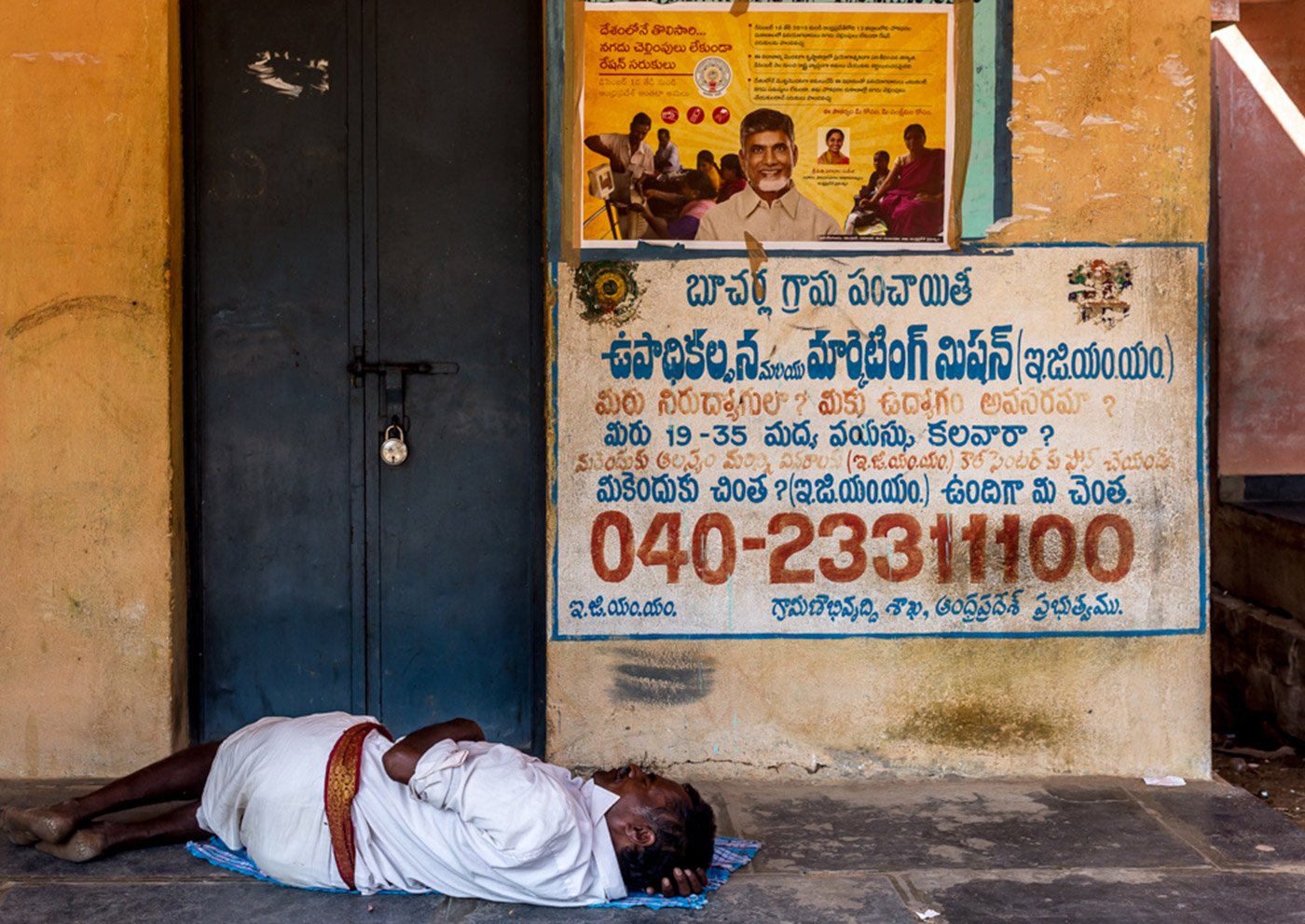 Writing on the wall: an out-of-work Dalit man rests outside the ration store in Bucharla. Ironically, a government helpline number for the jobless is painted on the wall 