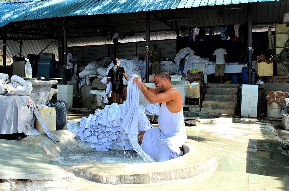 A washerman washing clothes inside the cement tubs at the ghat.