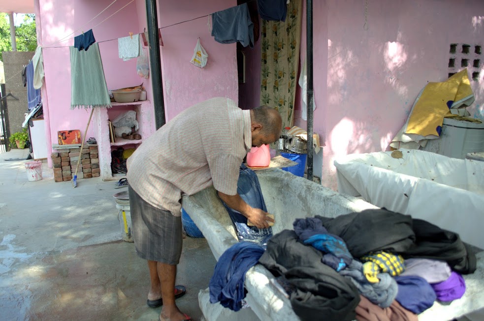 A washerman scrubbing clothes with detergent before washing them. 