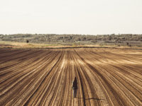 Young woman standing on the empty plowed field and looking away at the view
