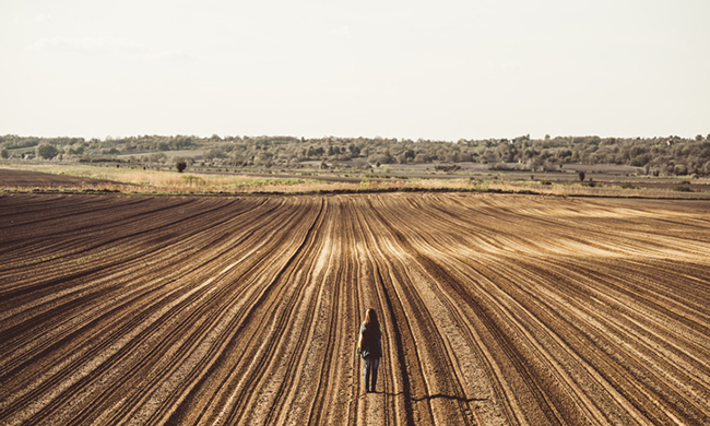 Young woman standing on the empty plowed field and looking away at the view