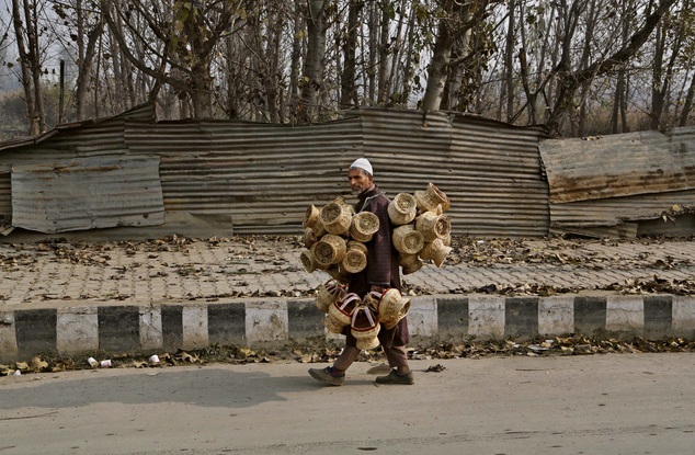 An elderly Kashmiri vendor sells Kangris or fire pots, on a cold morning in Srinagar, India, Monday, Nov. 24, 2014. Kangri is an age old device for keeping warm, consisting of a decoratively woven yellow wicker case housing an earthen pot for burning charcoal. (AP Photo/Mukhtar Khan)